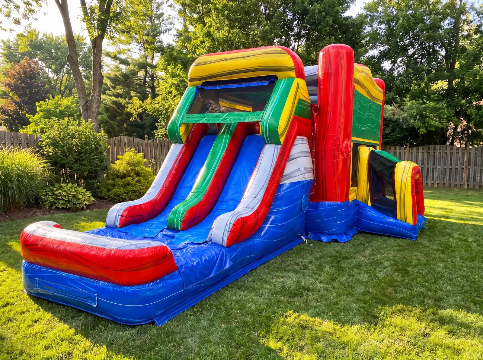 Colorful Slide/House Combo set up in a grassy backyard: a red, yellow, green and blue bounce house with a two-lane slide